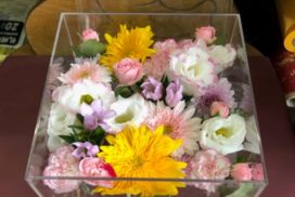 アクリルケースに収められている、白いトルコキキョウや黄色のガーベラなどの花々。