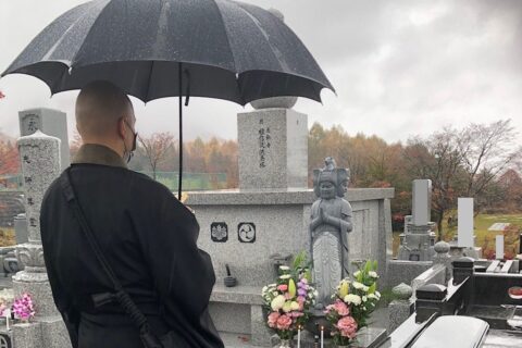 雨天の中ペットの合葬墓の前で読経をしている仏教の僧侶。