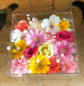 アクリルケースに収められた黄色とピンクと白のお別れ用の花々。