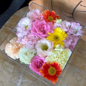 アクリルケースに収められた白とピンクと黄色のお別れ用の花々。
