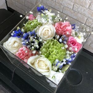 アクリルケースに収められた白とピンクと青のお別れ用の花々。