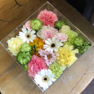 アクリルケースに収められた白と黄色とピンクのお別れ用の花々。