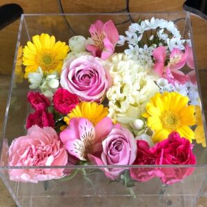 アクリルケースに収められた黄色とピンクと白のお別れ用の花々。