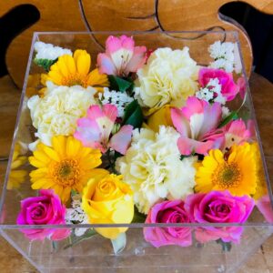 アクリルケースに収められたピンクと白と黄色のお別れ用の花々。