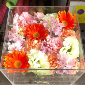 アクリルケースに収められた橙色とピンクと薄ピンク色のお別れ用の花々。
