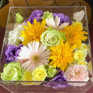 アクリルケースに収められた橙色と黄緑と薄紫のお別れ用の花々。