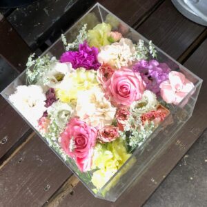 アクリルケースに収められた、ピンクのカーネーションや紫色のトルコキキョウなどの花々。