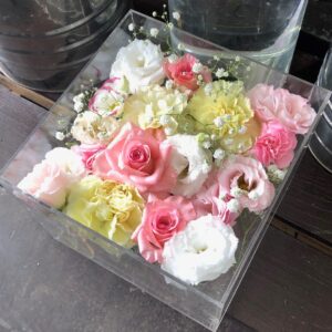 アクリルケースに収められた、ピンクの薔薇や白いカーネーションなどの花々。